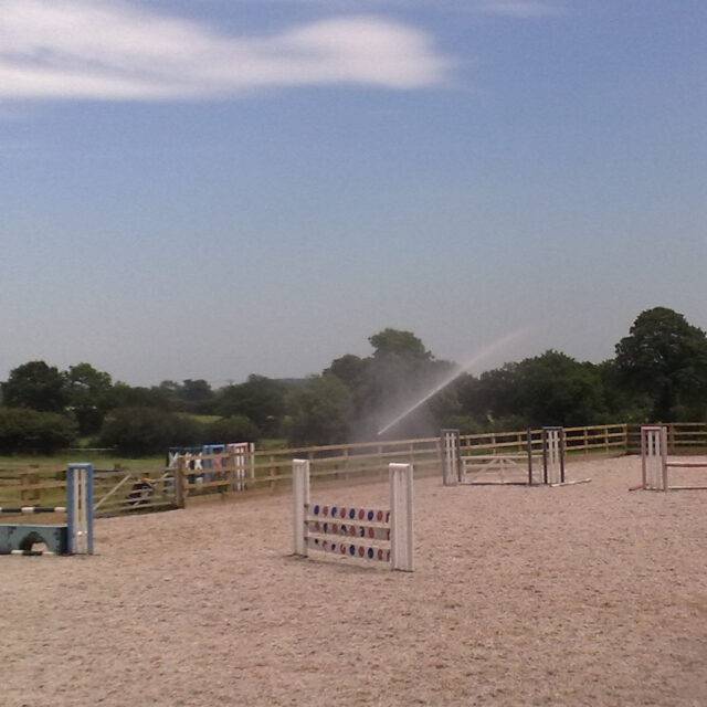 Large sprinkler watering horse arena to reduce dust problems for both horse and rider